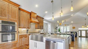 A spacious kitchen with wooden cabinets, stainless steel appliances, and pendant lighting. - Grovenor. Sleeps 14. Family Home. Triple Garage. (Edmonton)