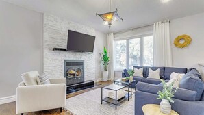 A modern living room with a fireplace, a flat-screen TV, a sofa, and a coffee table. - Grovenor. Sleeps 14. Family Home. Triple Garage. (Edmonton)