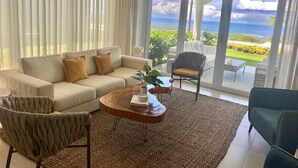Un salon moderne comprenant un canapé, des fauteuils, une table basse et offrant une vue sur l’océan grâce à de grandes portes coulissantes.
