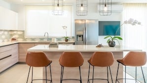 Une cuisine moderne dotée d’un îlot central, de luminaires suspendus et de tabourets de bar.
