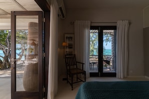 Una habitación con una cama, una silla, una mesa y vistas a la playa y al océano a través de la puerta.