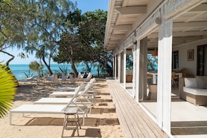 Un salón junto a la playa con sillones blancos y una terraza de madera con vistas al océano.