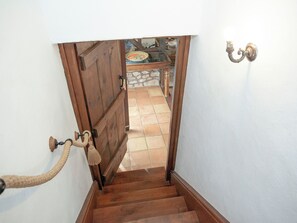 Una escalera de madera con un pasamanos de cuerda que lleva a un cuarto con piso de baldosas y una mesa con vajilla.