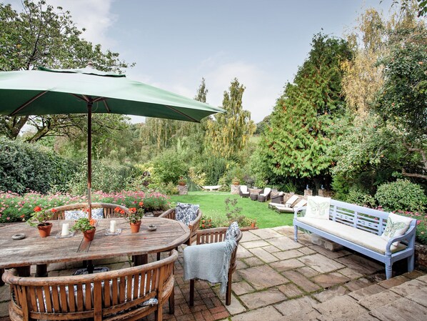 A wooden patio with a round table and chairs, a bench, and a green umbrella.