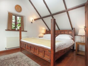 Un dormitorio con una cama de madera con dosel, una ventana con cortinas, un radiador y una mesita de noche con una lámpara.