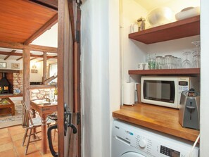 A kitchen with a washing machine, microwave, and shelves with dishes and glasses.