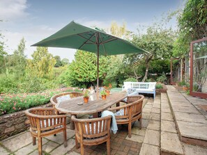 A patio with a table and chairs, surrounded by a garden with various plants and flowers.