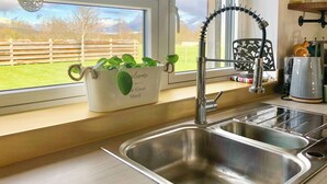 A kitchen with a stainless steel sink, a window with a view of a fenced yard, and a white container with green plants. - 2 bedroom accommodation in Hadlow, near Tonbridge (Hadlow, near Tonbridge)