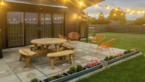 An outdoor patio with a wooden table and chairs, string lights, and planters. - 2 bedroom accommodation in Hadlow, near Tonbridge (Hadlow, near Tonbridge)