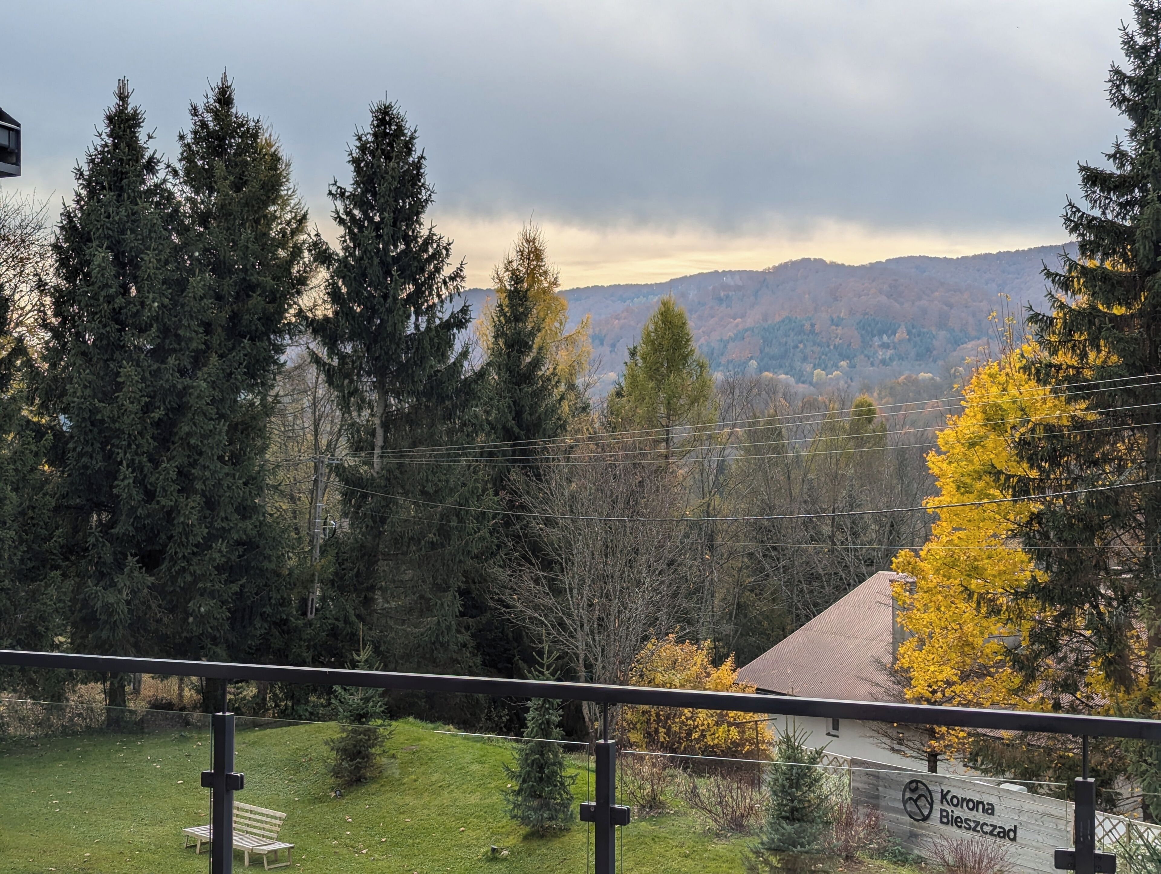 Vista de una zona residencial con una casa, un banco y un letrero que dice 'Korona Bieszczad'.