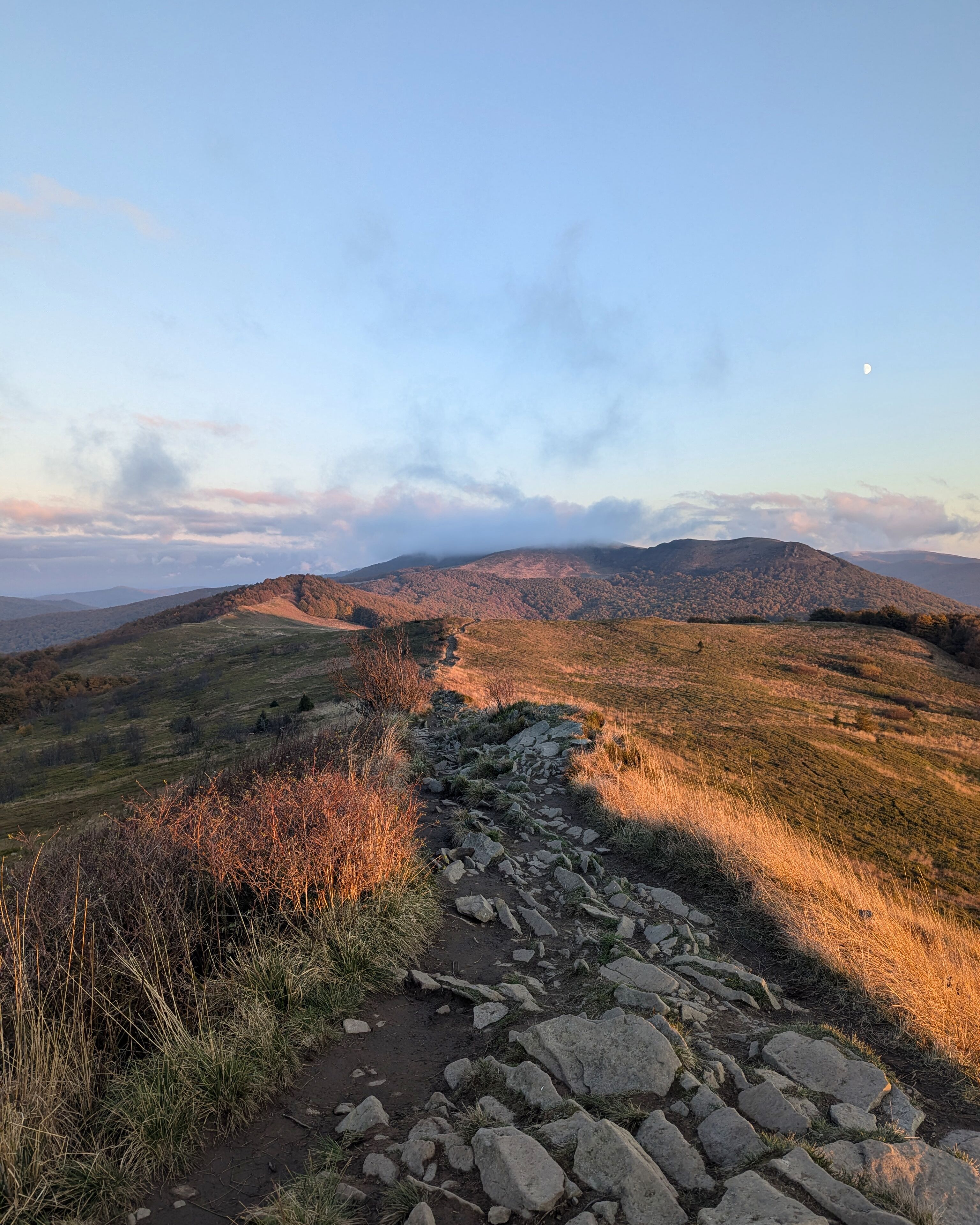 A rocky path leading through a hilly landscape with a clear sky and a visible moon.