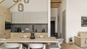 A modern kitchen with a wooden dining table, white chairs, and a coffee machine. - Korona Bieszczad Premium Apartments (Cisna)