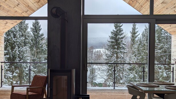 A modern interior with large windows, a fireplace, and a view of snow-covered trees. - Korona Bieszczad Premium Apartments (Cisna)