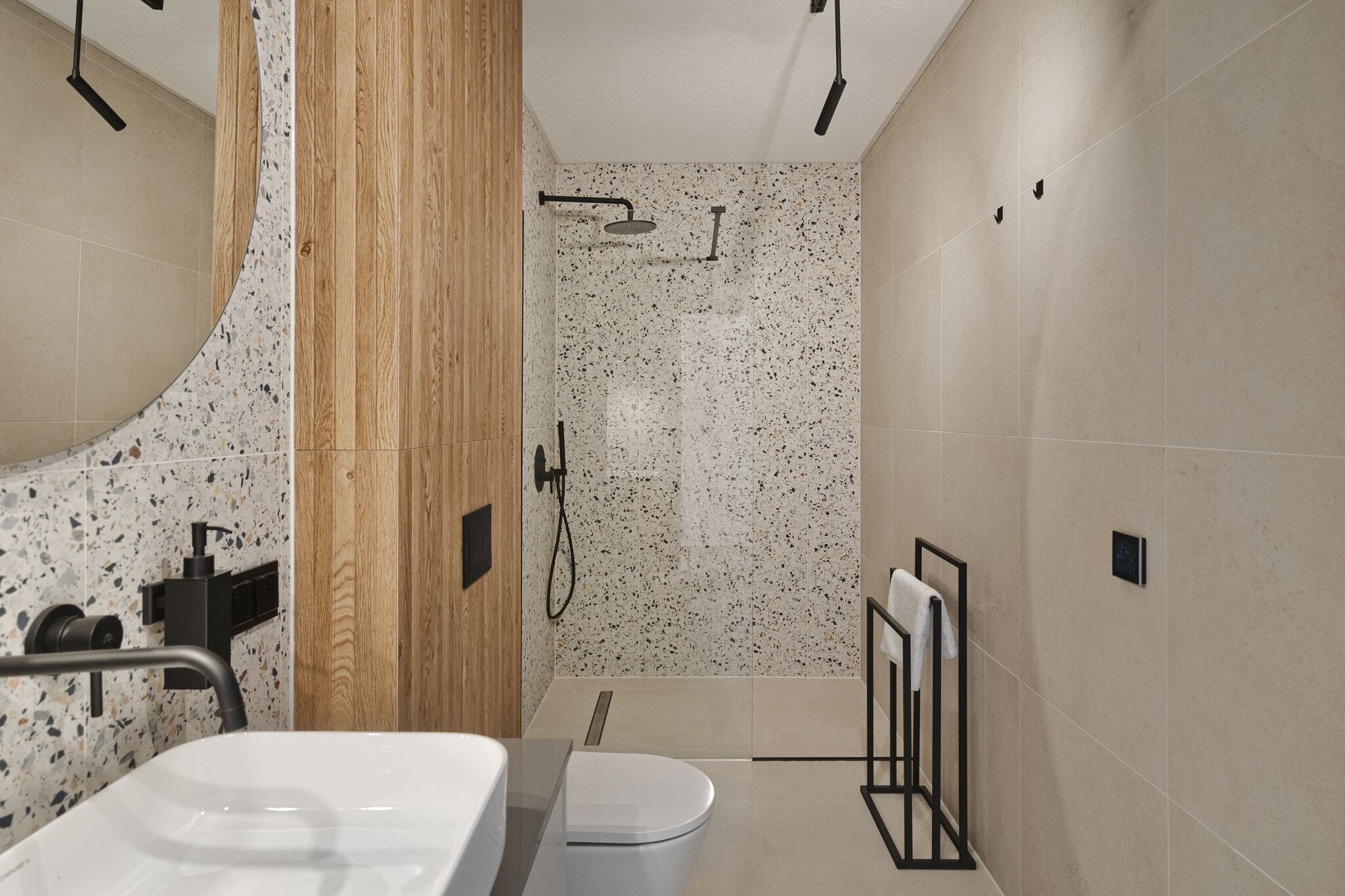 Een moderne badkamer met een vrijstaand bad, een toilet en een douchegedeelte met een betegelde muur met stippen.