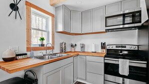 A modern kitchen with grey cabinets, a wooden countertop, a stainless steel stove, and a microwave. - Hygge Up North Bungalow (Bellaire)