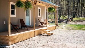 A wooden cabin with a porch, two rocking chairs, and hanging plants. - Hygge Up North Bungalow (Bellaire)