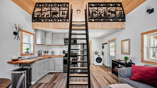 A loft-style living space with a central wooden ladder, a kitchen with modern appliances, and a cozy seating area. - Hygge Up North Bungalow (Bellaire)