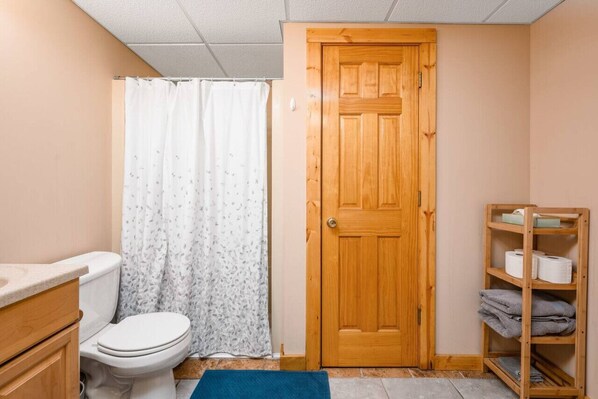 Une salle de bain avec des toilettes, un rideau de douche, une porte en bois et une étagère avec des serviettes.