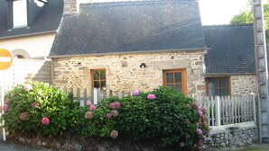 Ett stenhus med ett trästaket och rosa blommor.