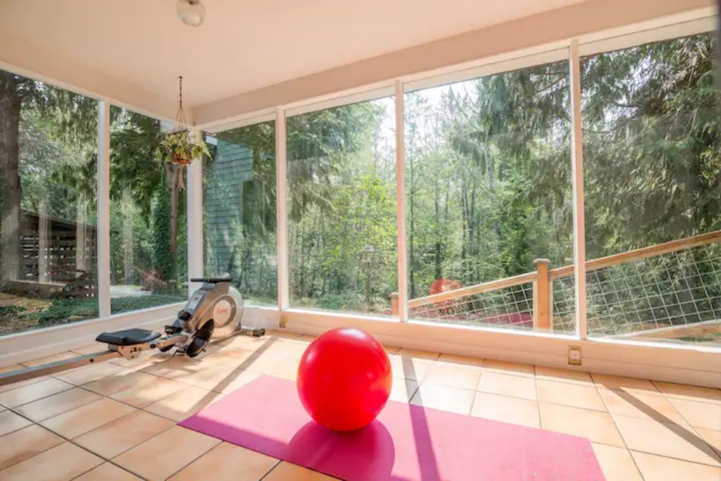 A spacious room with large windows, a stationary bike, and a red exercise ball on a pink mat.