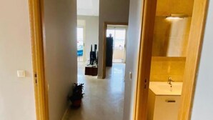 Un pasillo con una puerta de madera a la derecha, que da a un baño con lavamanos y espejo.