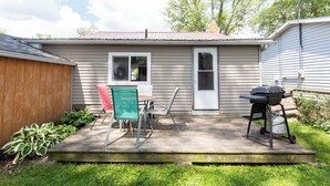 Een klein huis met een terras, een barbecue en een tafel met stoelen.