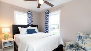 Een slaapkamer met een bed, nachtkastje, stoel en plafondventilator.
