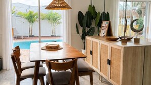 A dining area with a wooden table and chairs, a glass cabinet, and a view of a swimming pool. - Tropical Vacation POOL Home in Melbourne, 7 mins to Beach (Melbourne)