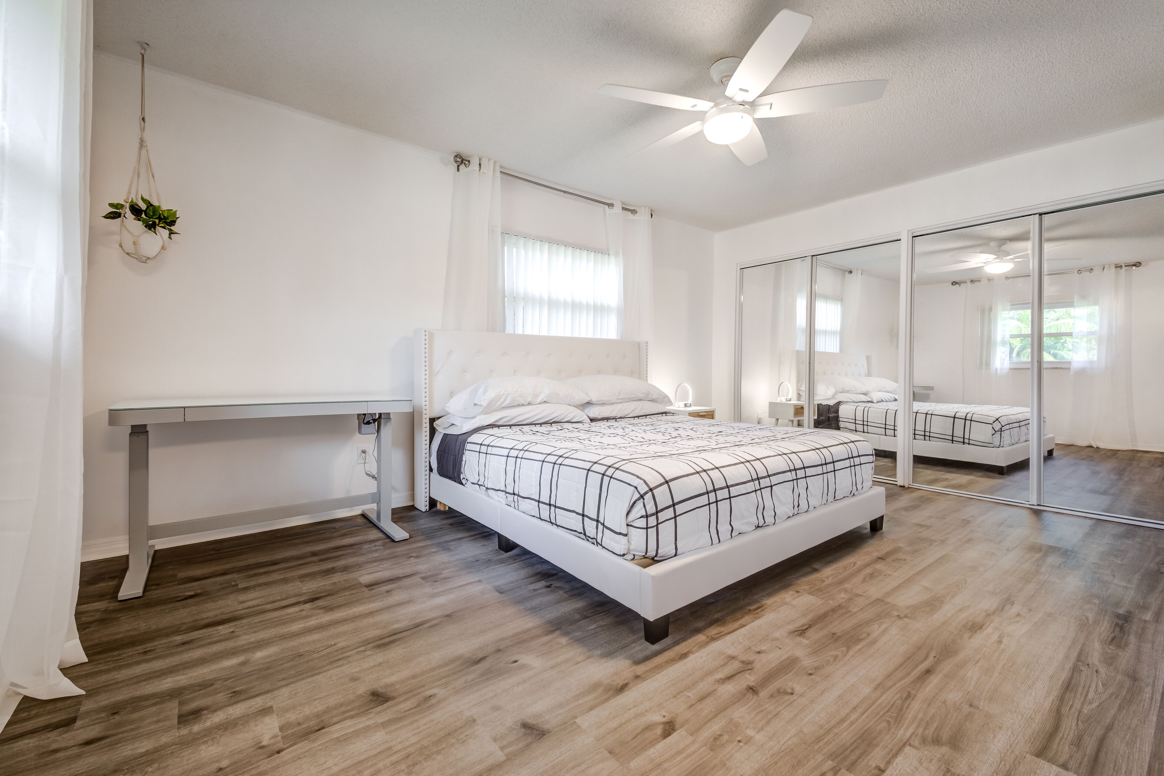 A bedroom with a bed, a desk, a ceiling fan, and a large mirror.