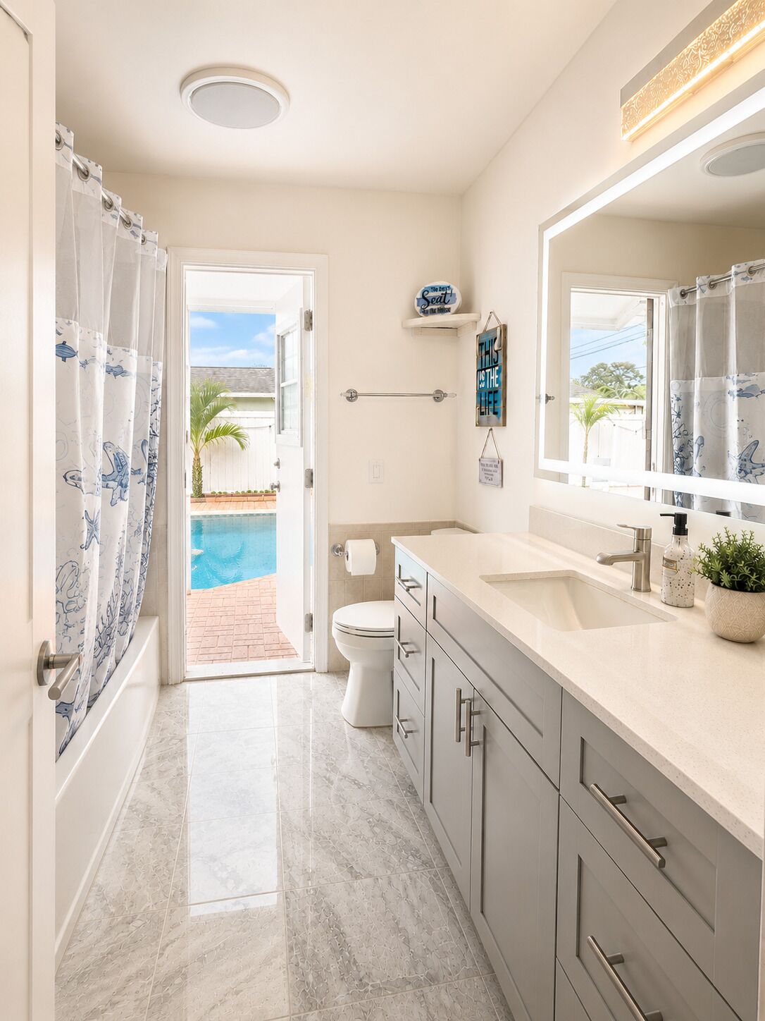 Une salle de bain avec un sol en marbre, des toilettes, un lavabo et une douche donnant sur une piscine et des palmiers.