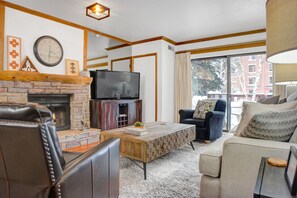 Cozy living room with a fireplace, comfortable seating, and a large window offering a view of the outside.