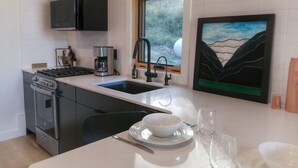 Eine moderne Küche mit Gasherd, Kaffeemaschine und Spüle. Ein Fenster bietet Blick auf Grünfläche.