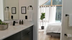 Ein modernes Badezimmer mit einem großen Spiegel, zwei gerahmten Schildern, einem Waschbecken mit zwei Flaschen und einer Topfpflanze.