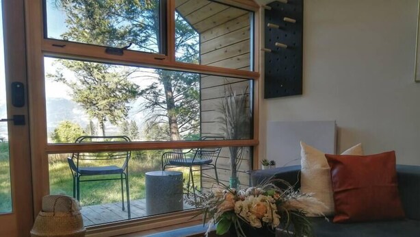 Ein modernes Wohnzimmer mit einem großen Glasfenster, das in einen Außenbereich führt, einem blauen Sofa, einem Holztisch mit Blumen und einem gewebten Korb.