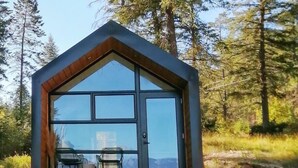 Eine Holzhütte mit großem Fenster, einer Holzterrasse und zwei Stühlen.