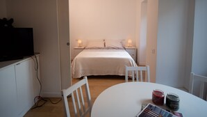 Une chambre à coucher avec un lit, des tables de chevet avec des lampes, un téléviseur posé sur un meuble et une table sur laquelle se trouvent divers objets.