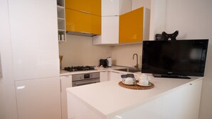 Une cuisine moderne avec des meubles blancs et jaunes, une cuisinière à gaz, un évier et un téléviseur à écran plat.