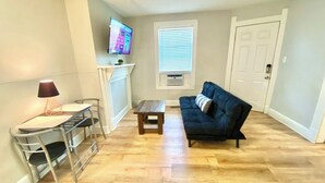 Un salon avec un canapé, une petite table, un téléviseur fixé au mur et une porte.