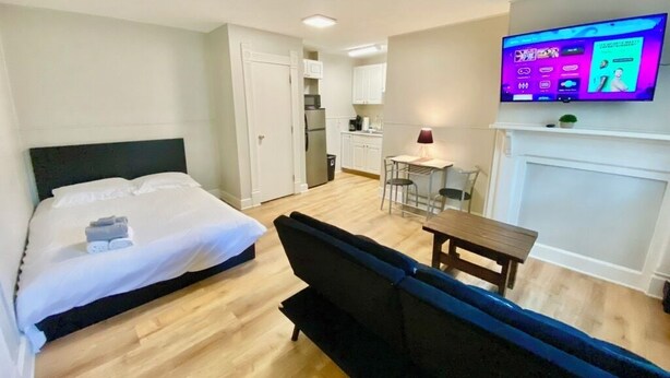 Une chambre d’hôtel avec un lit, un canapé, une télévision, une petite table et, au fond, une kitchenette.