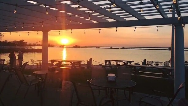 An outdoor seating area with tables and chairs, overlooking a body of water during sunset. - Condo with Lake & Cedar Point View (Sandusky)