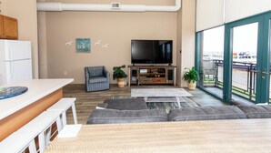 A modern living room with a large TV, grey sofas, a wooden coffee table, and a view of the harbor through large windows. - Condo with Lake & Cedar Point View (Sandusky)