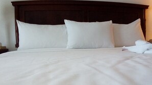 A neatly made bed with white linens and pillows, a wooden headboard, and a white towel on the side. - Condo GV (Puerto Vallarta)