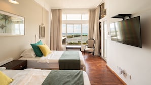 Ein Hotelzimmer mit zwei Betten, einem Fernseher, einem Sessel und Blick auf das Meer.