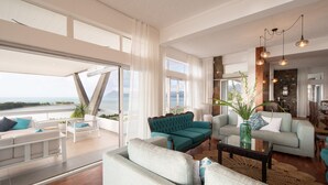 Ein geräumiges Wohnzimmer mit Meerblick, ausgestattet mit einem hellblauen Sofa, einem türkisblauen Sofa und einem weißen Sofa.