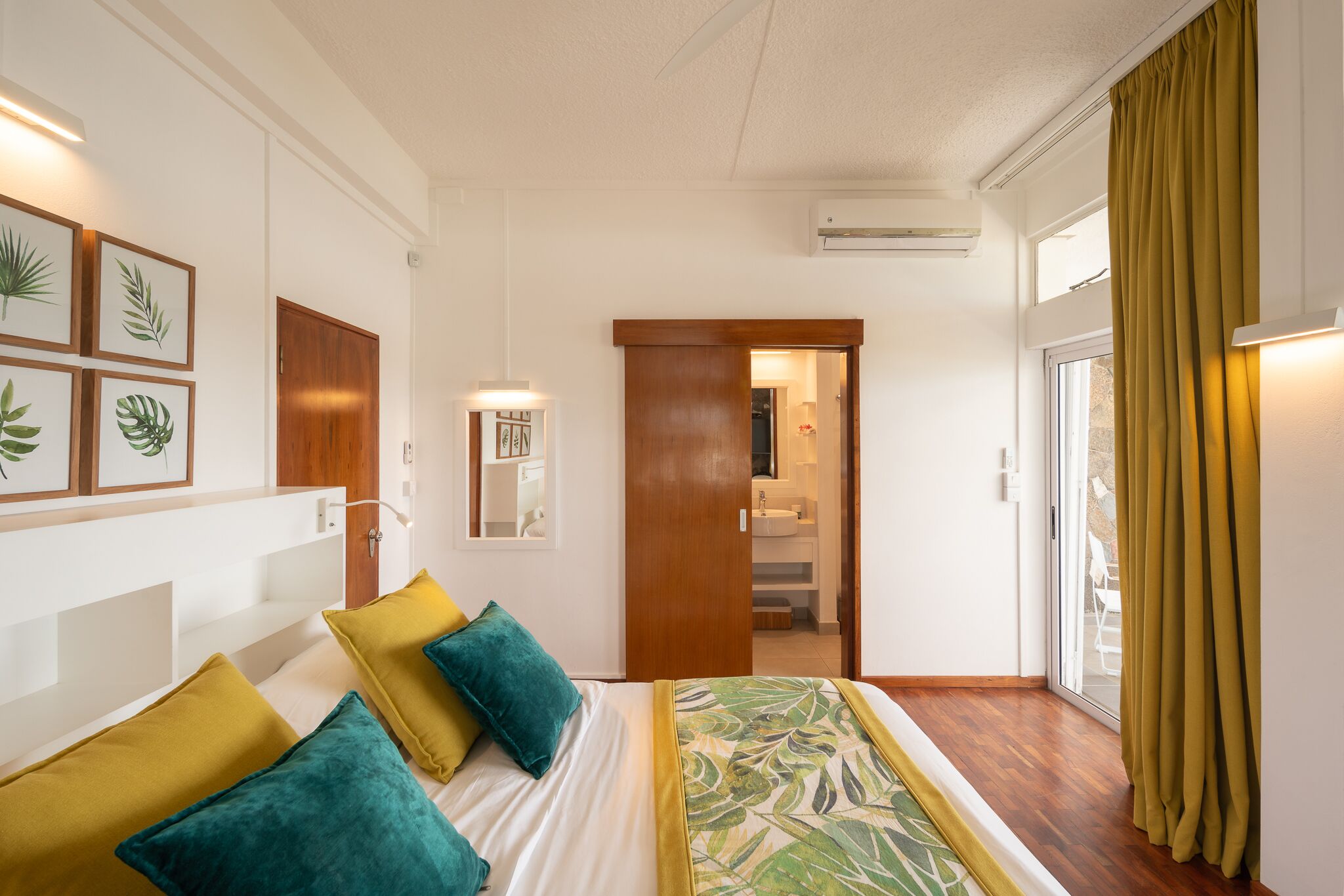 A bedroom with a bed, pillows, a nightstand, a mirror, and a door leading to a bathroom.
