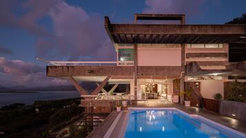 A modern house with a pool, large windows, and a view of the sea.