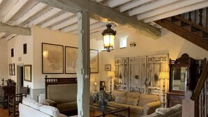 A spacious living room with a high ceiling and exposed beams, furnished with white sofas and a coffee table.