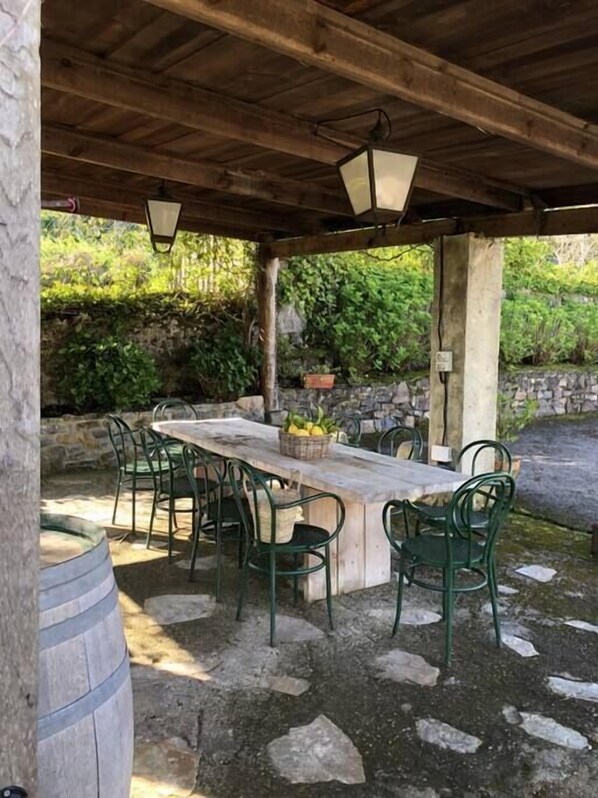 An outdoor patio with a wooden table and chairs, stone walls, and greenery in the background. - Beautiful Stone House, La Llosuca (AS)