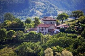 A traditional building with a red-tiled roof, surrounded by lush greenery and hills in the background. - Beautiful Stone House, La Llosuca (AS)