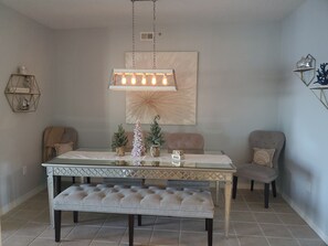 A dining area with a glass table, a bench, and a hanging light fixture. - Pensacola beach condo, perfect location, w sunset water views (Pensacola Beach)